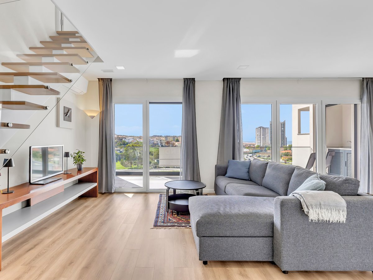 The open living area of the Buarcos duplex, with the staircase to the upper floor and the sea beyond