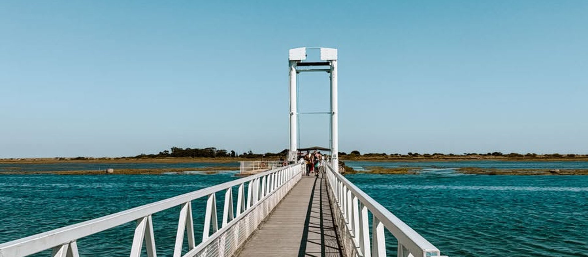 A long white footbridge running out across the calm water of the Ria Formosa