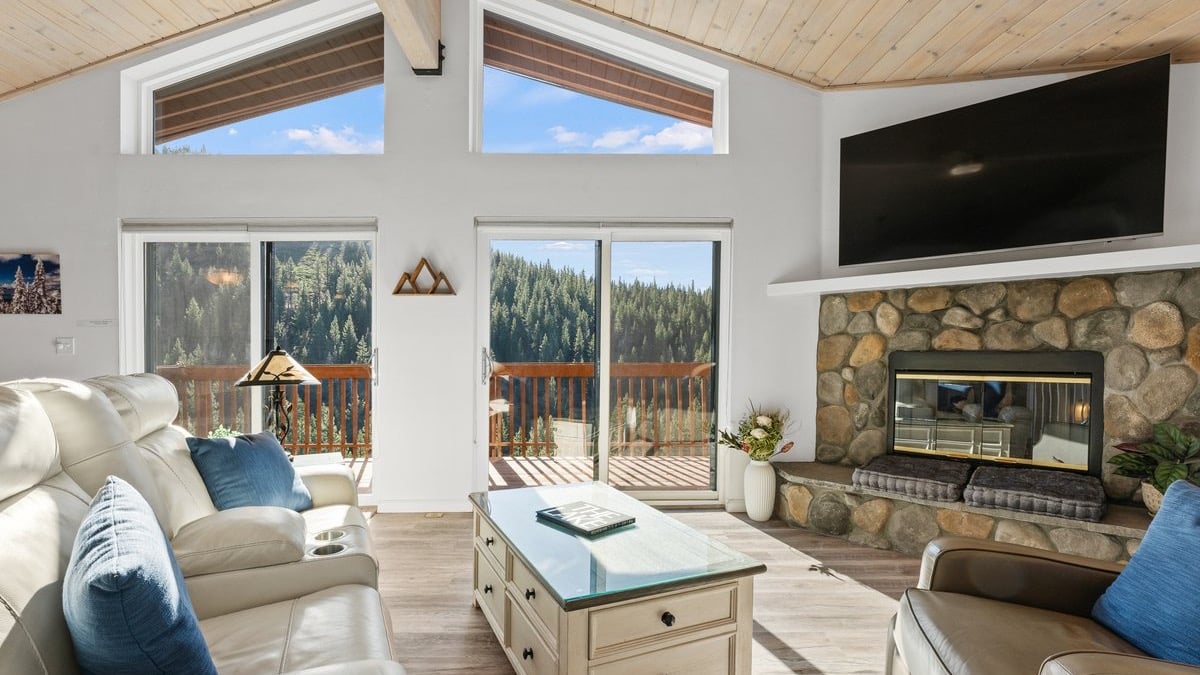 Bright great room with a vaulted wood ceiling, a stone fireplace, sofas and sliding doors to a deck in a Bitterbrush condominium