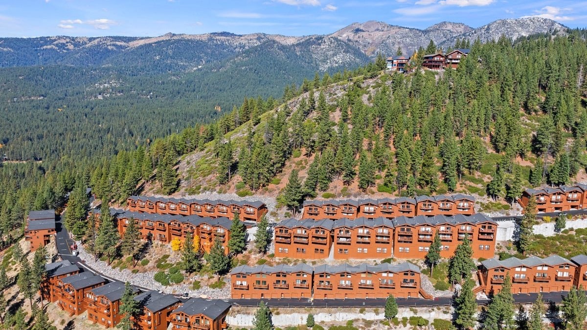 Aerial view of rows of brown wood-sided Bitterbrush condominium buildings on a forested hillside in Incline Village, with mountains behind
