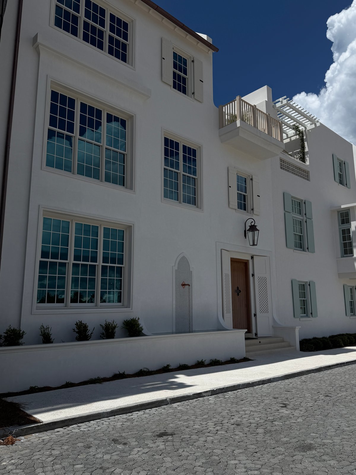 White Alys Beach home with tall windows, pale shutters, a wooden entry door and an upper terrace