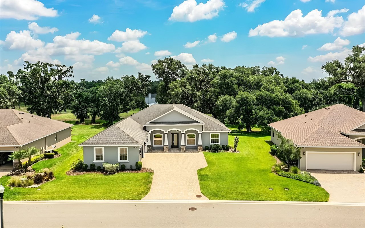 Single-story gray home with a covered entry and wide driveway, surrounded by green lawns and mature trees.