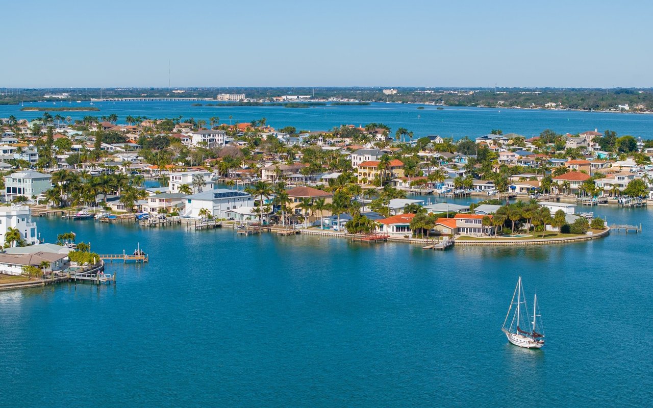 Aerial view of Treasure Island waterfront homes and canals, with a sailboat in the foreground.