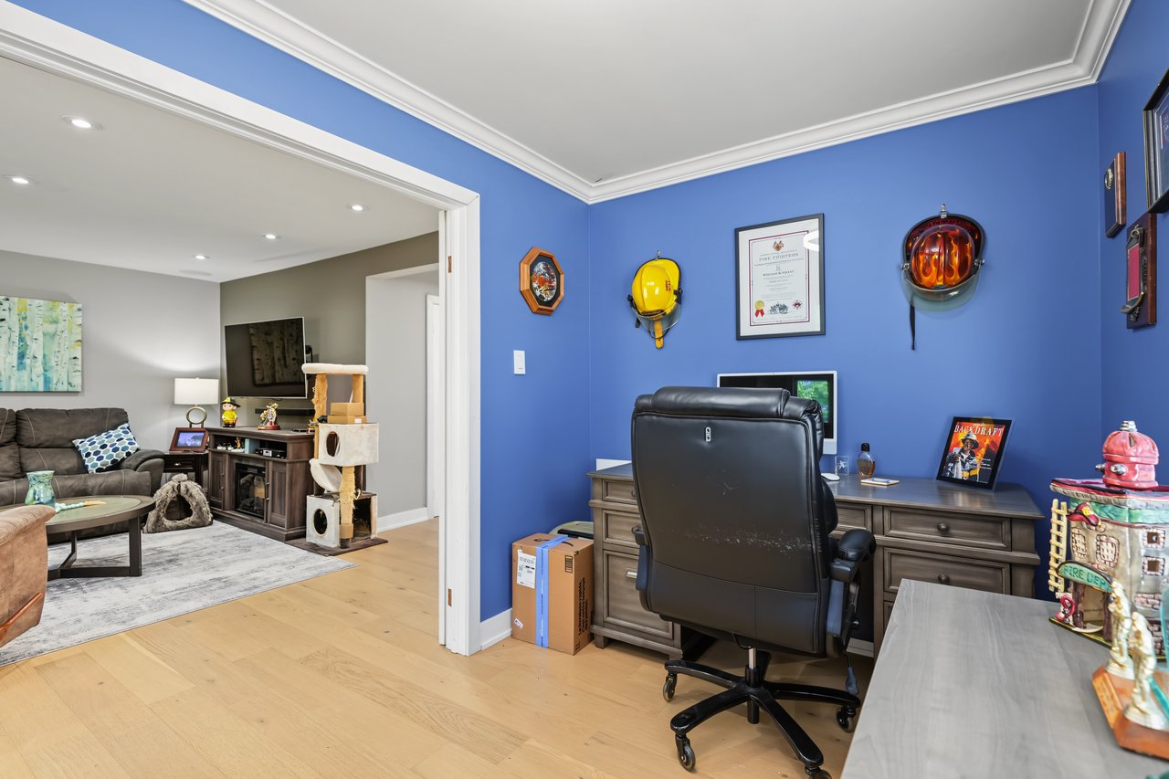 Furnished home office with blue walls and a large desk, opening into a living room.