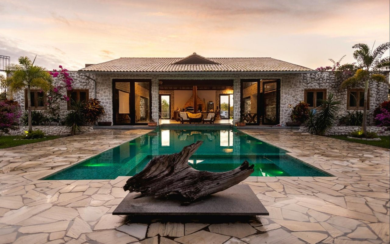 Stone-clad home with open glass doors, a pool, and a driftwood sculpture on the patio.