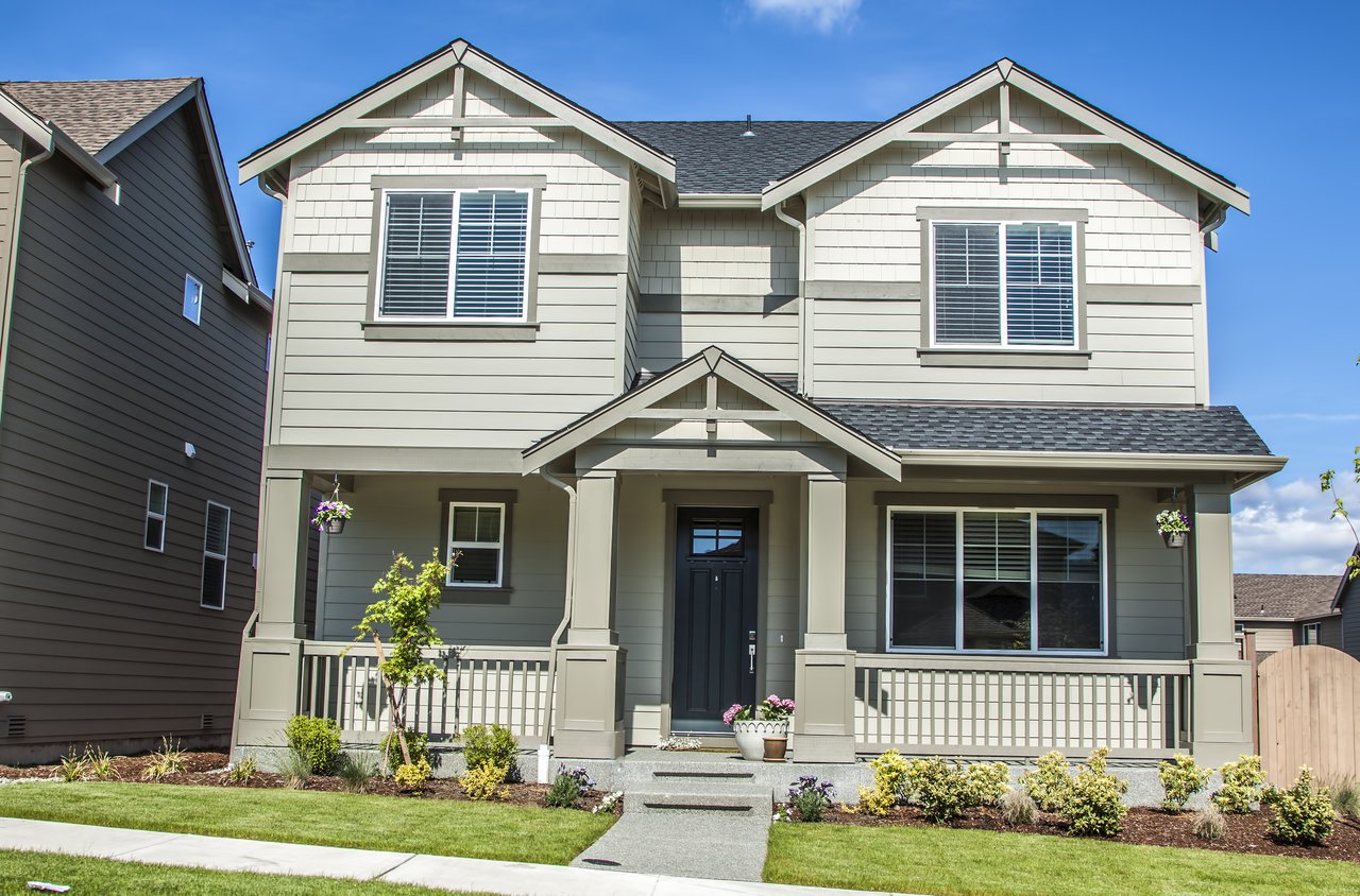 Two-story gray house with a covered porch, gabled roof, and landscaped front lawn.
