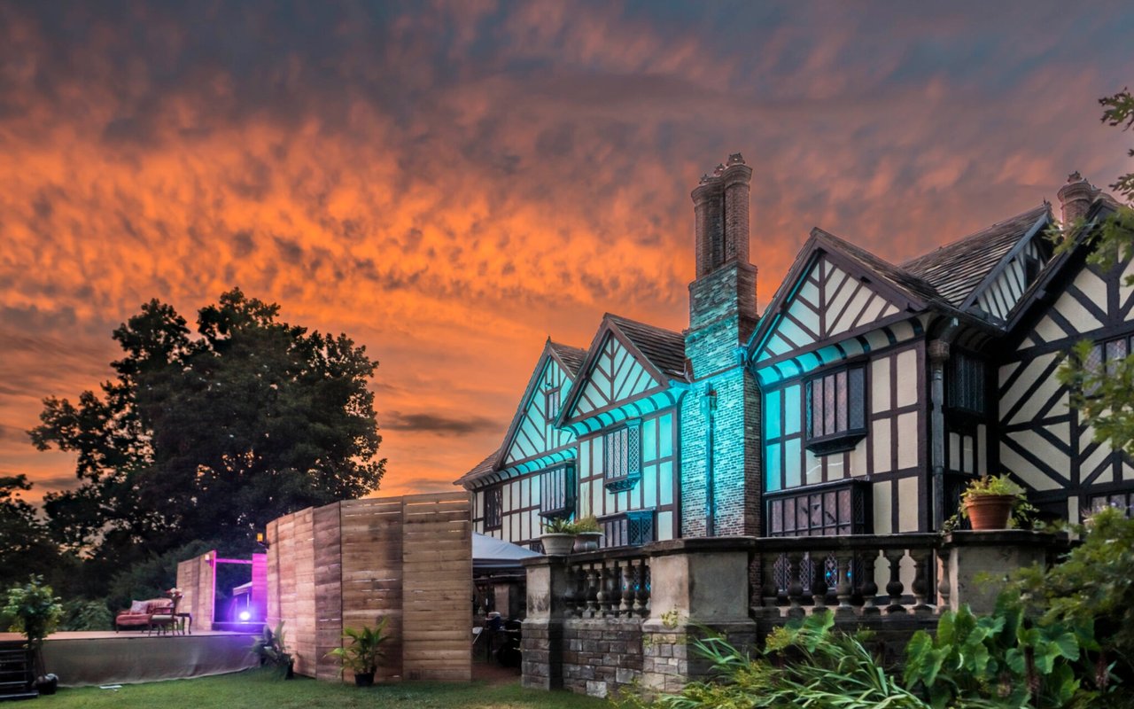 Tudor-style building and outdoor stage illuminated beneath an orange sunset.
