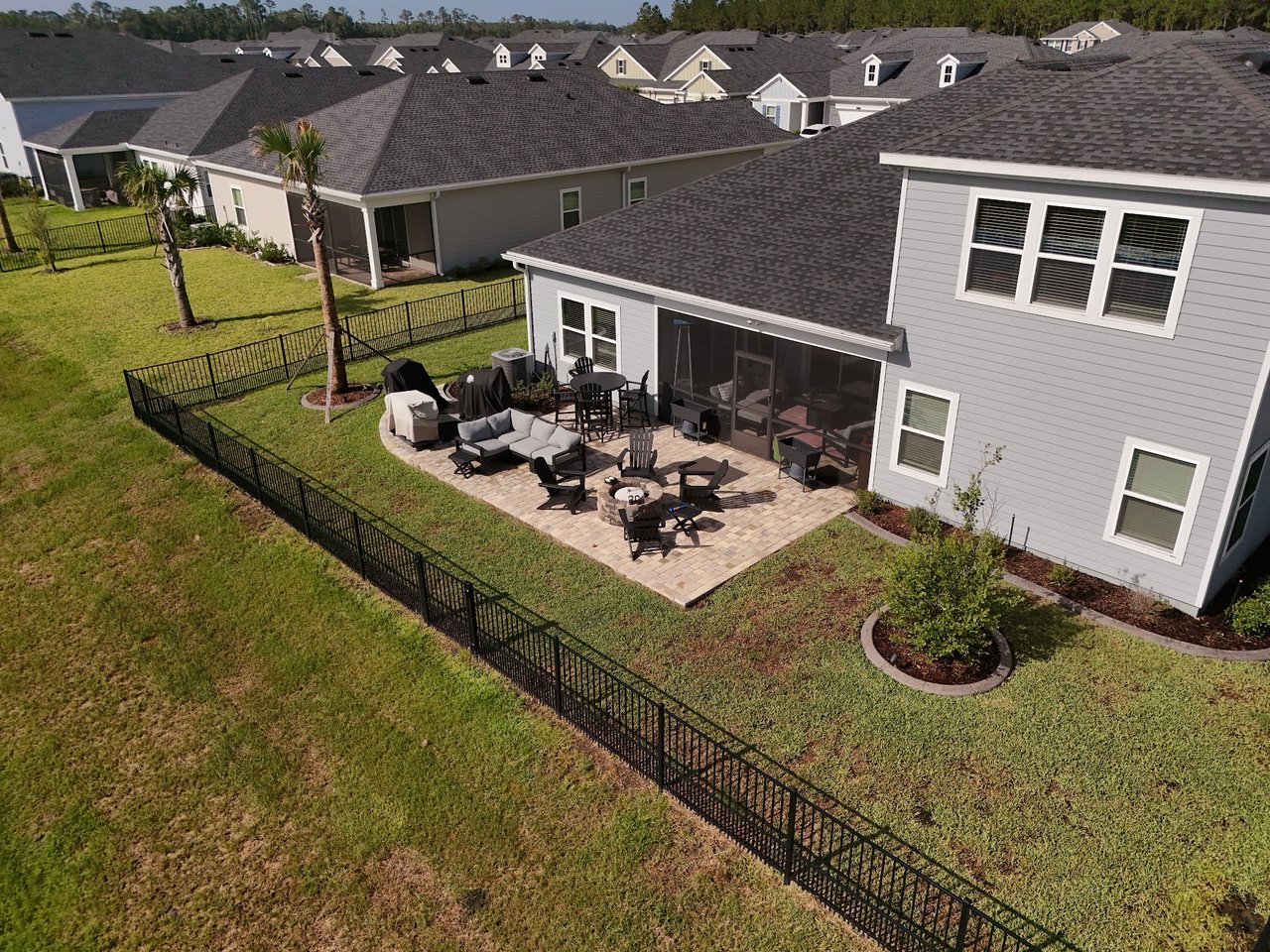 Aerial view of a gray home with a fenced backyard patio, outdoor seating, fire pit, and screened porch.