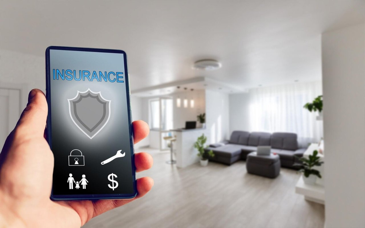 Smartphone displaying insurance and security icons in front of a modern living room.