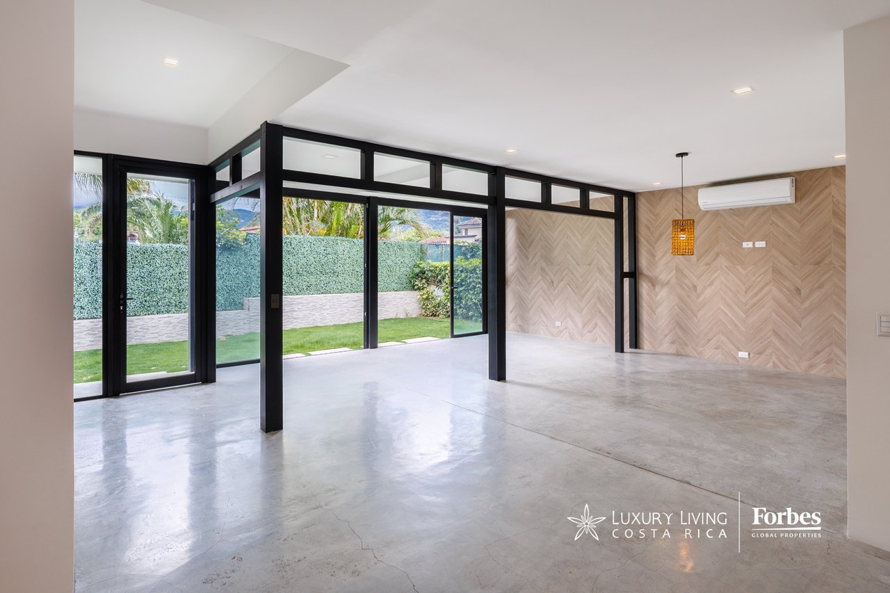 Vacant living area with black steel-framed glass walls, polished concrete floors, and garden views.