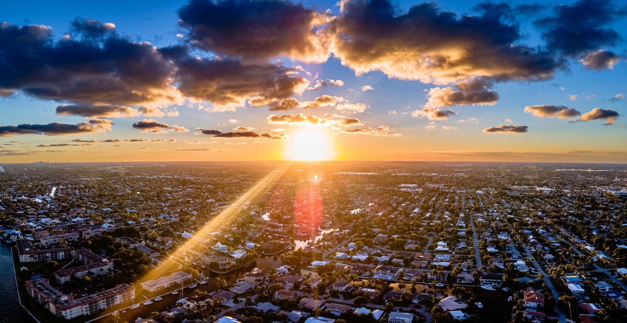 Aerial view of a residential neighborhood at sunset, with waterways and dramatic clouds.