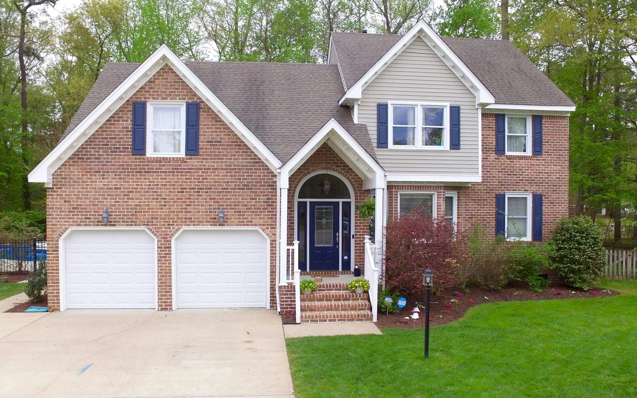 Two-story brick-and-siding house with blue shutters, a double garage, and landscaped front lawn.
