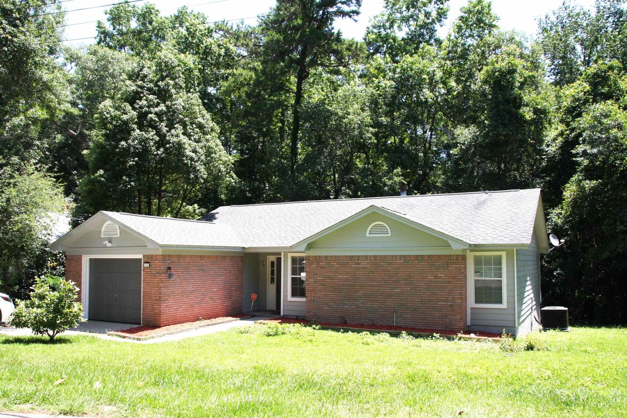 A brick home with a garage, surrounded by trees, set against a clear sky in the background.
