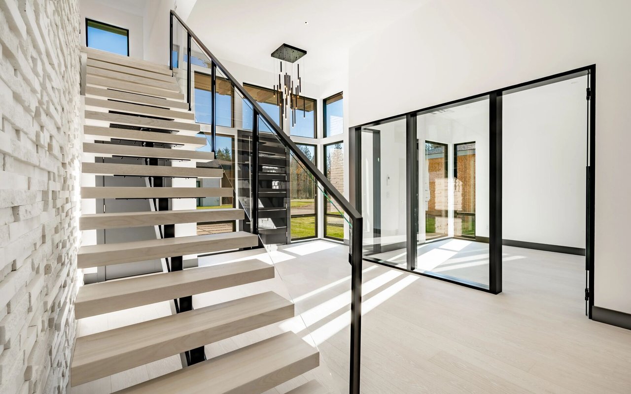Modern foyer with a floating wood staircase, black railings, and expansive glass doors.