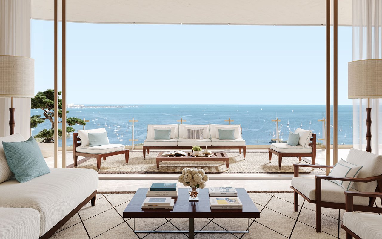 Furnished living room with floor-to-ceiling windows overlooking sailboats on the ocean.