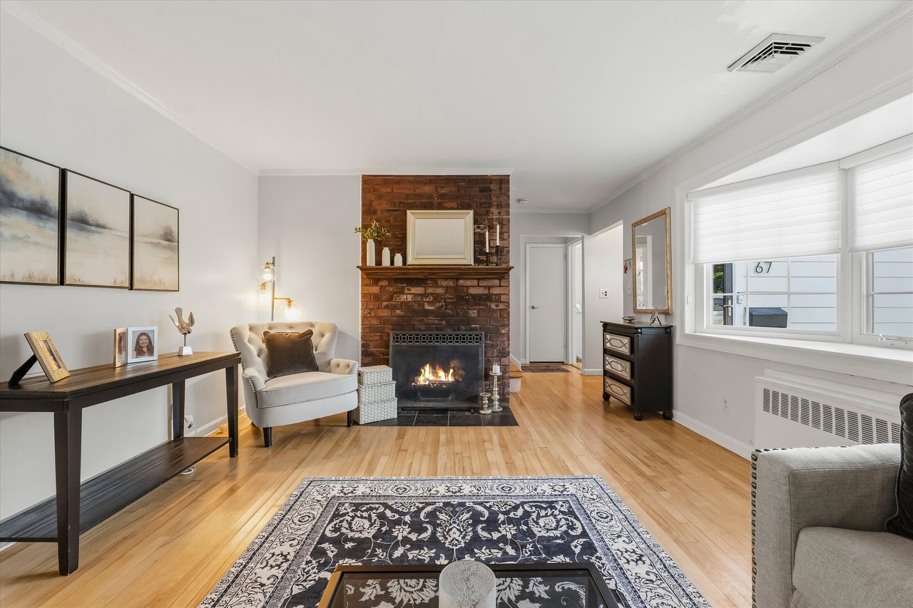 Living room with a brick fireplace, hardwood floors, and large windows with white blinds.
