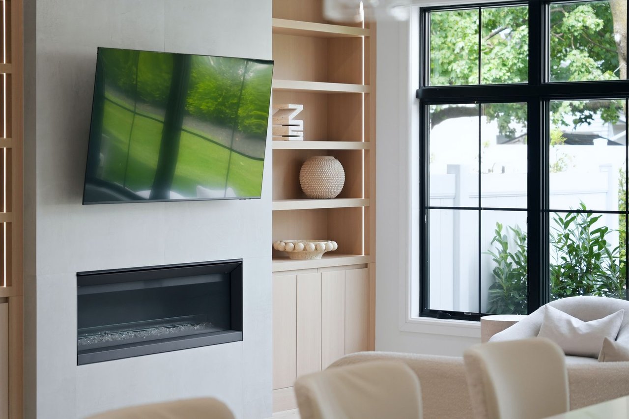 Living room with a linear fireplace, built-in shelves, and large windows overlooking greenery.