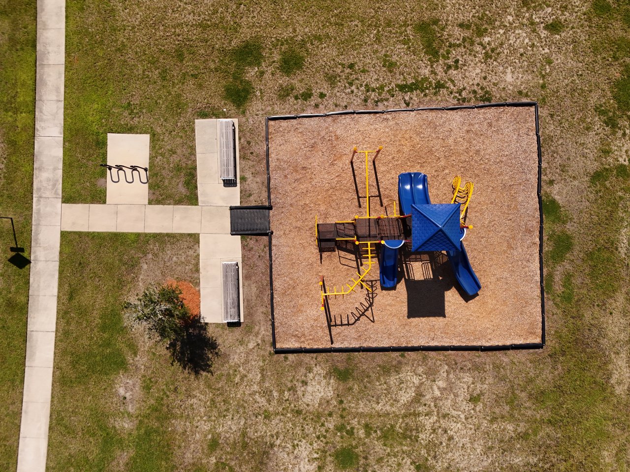 Aerial view of a neighborhood playground with blue slides and yellow climbing equipment.