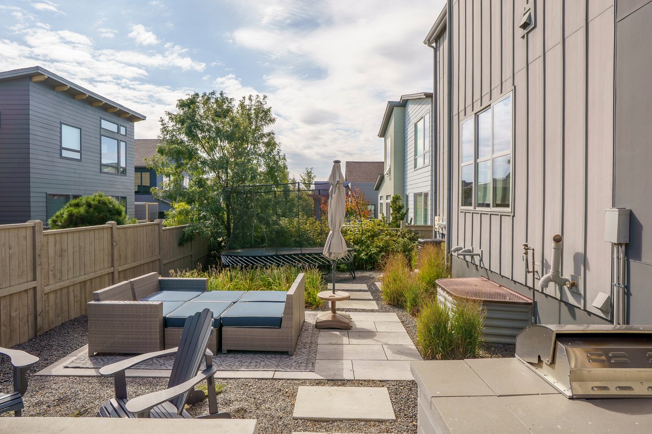Backyard patio with outdoor seating, Adirondack chairs, and a built-in grill along the fence