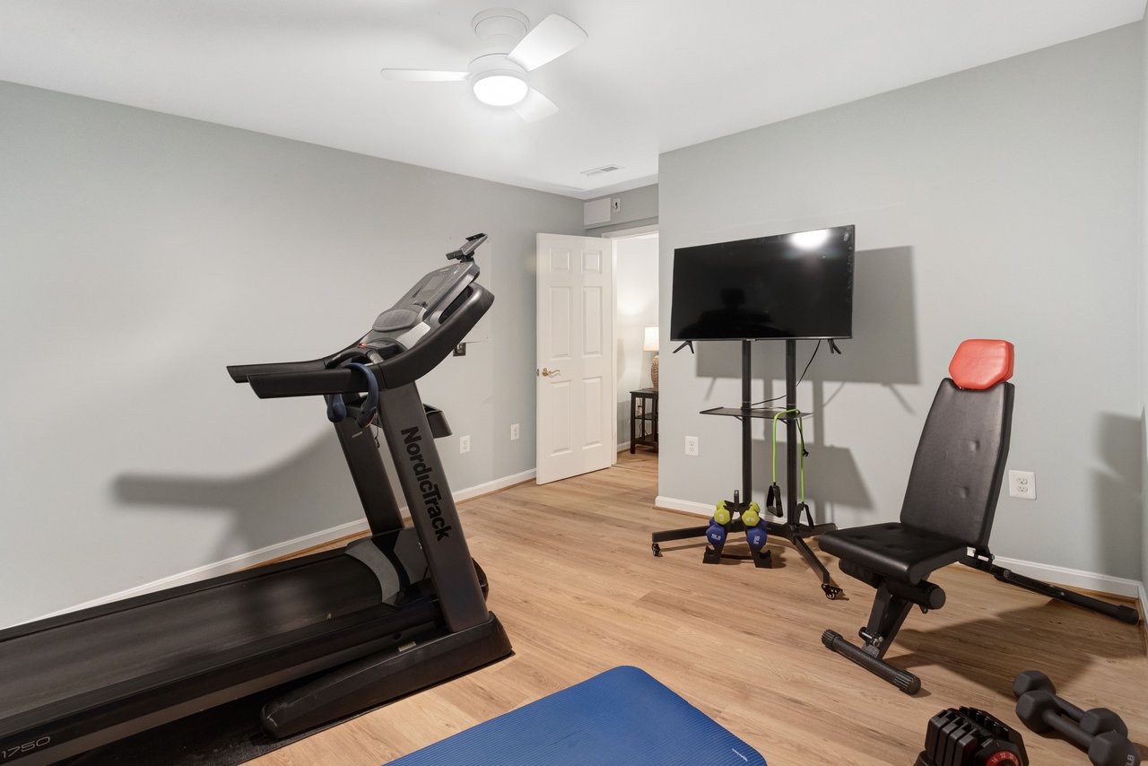 Home gym with a treadmill, weight bench, mounted television, and blue exercise mat.