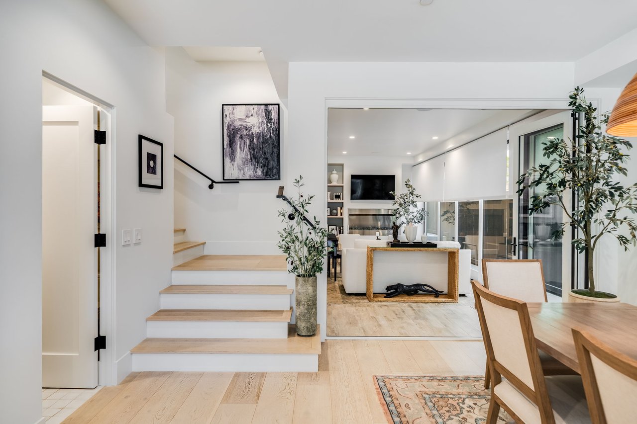 Furnished open-plan living and dining area with light wood floors, a staircase, and large glass doors.