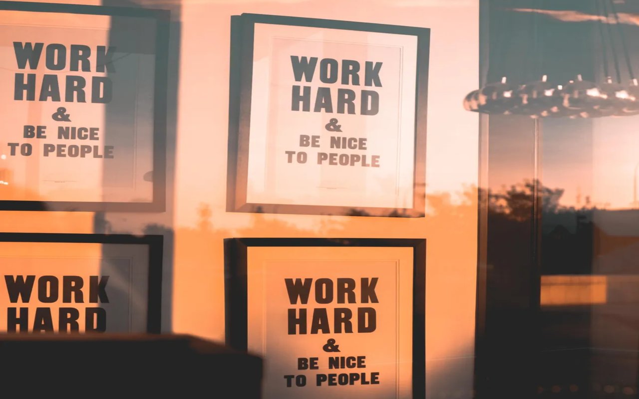 Several framed posters, each with the text "WORK HARD & BE NICE TO PEOPLE," are in a window, illuminated by a warm sunset.