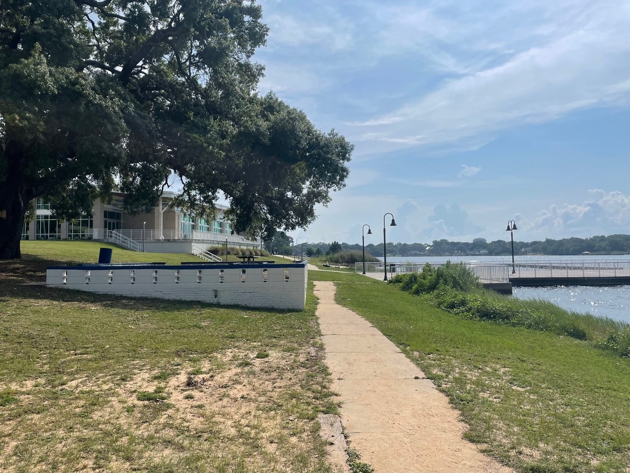 East Hill waterfront path beside a modern building, shaded by oak trees and leading to a bayfront promenade.
