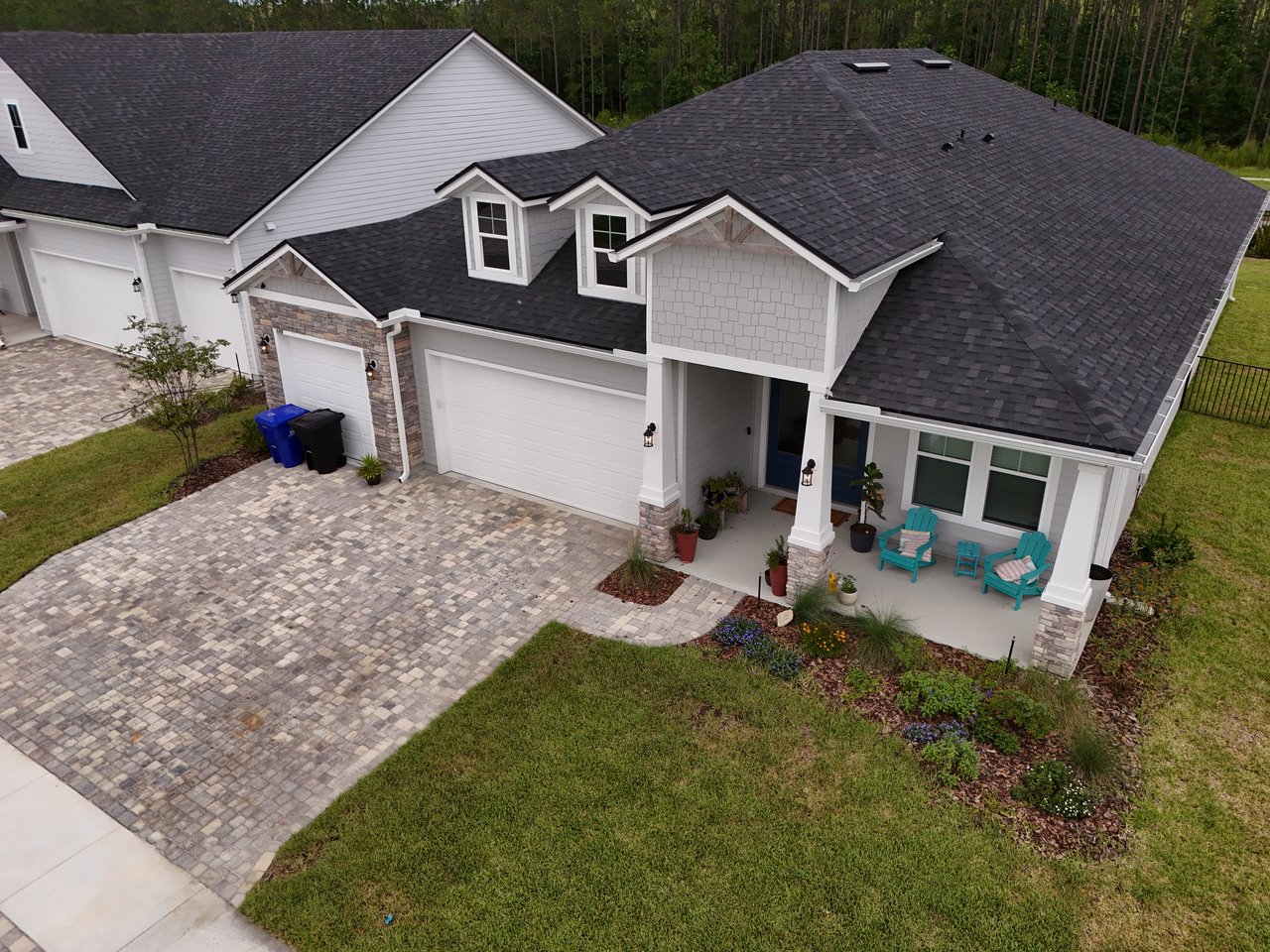 Aerial view of a white home with a paver driveway and covered porch with turquoise chairs.