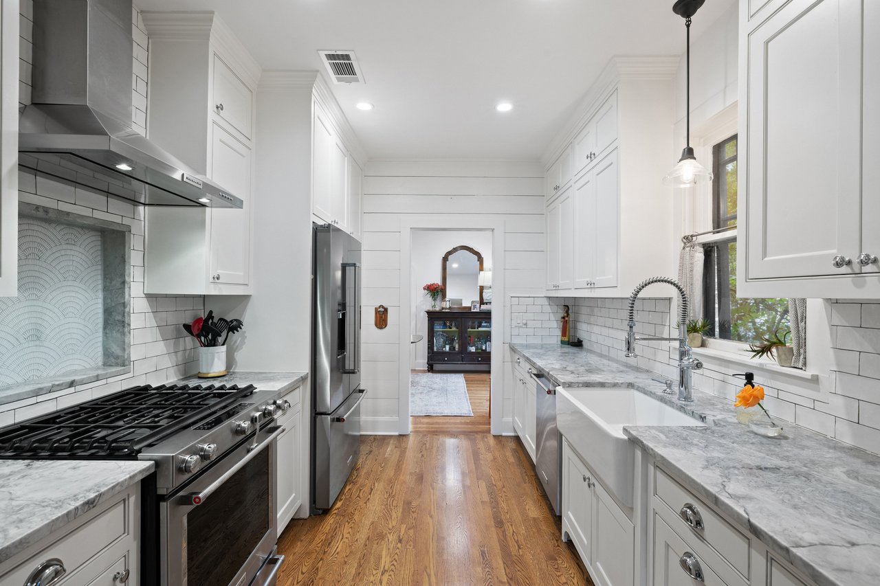 Kitchen with white cabinets, marble counters, farmhouse sink, stainless appliances, and wood floors.