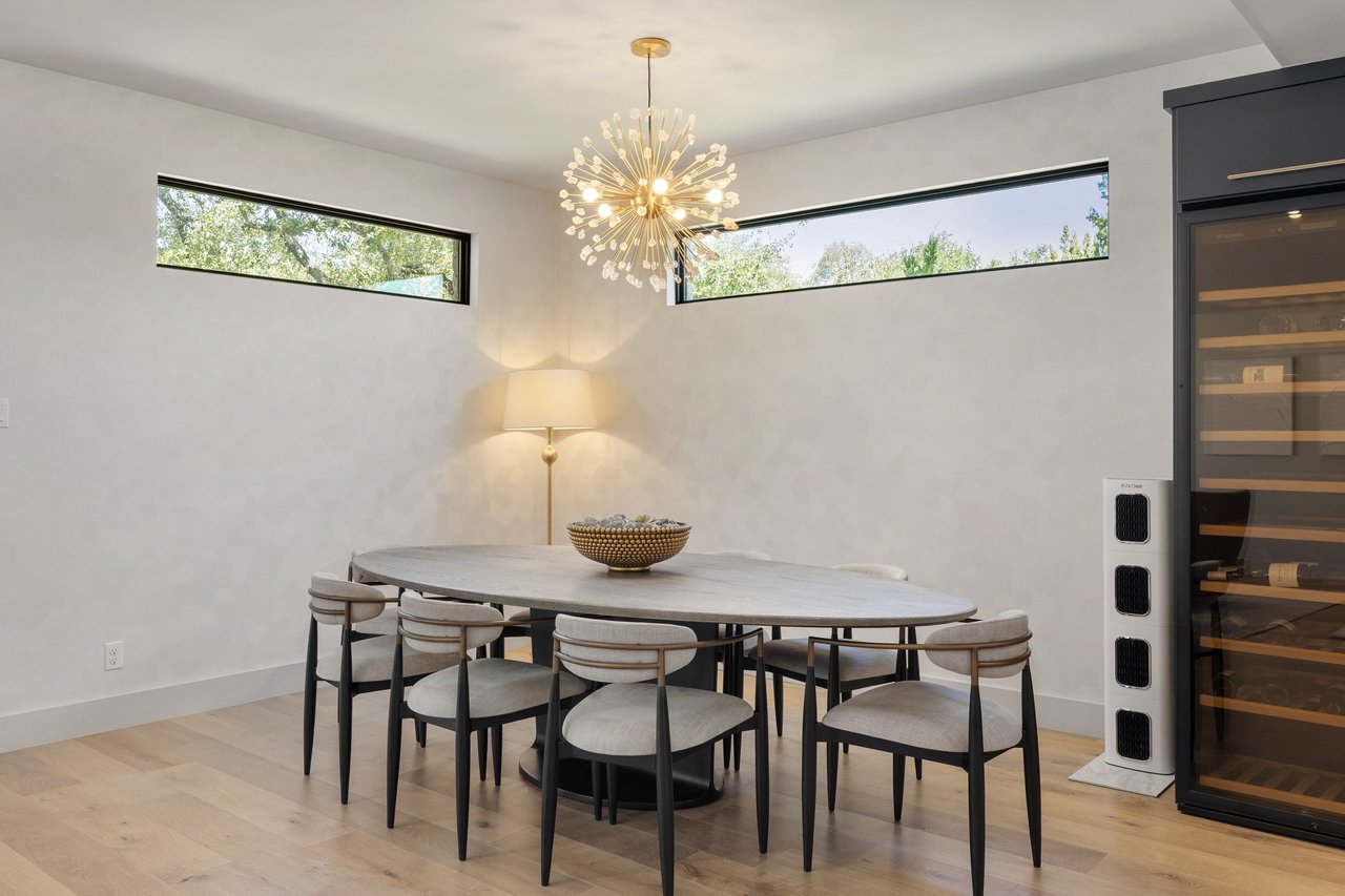 Dining room with an oval table, sculptural chandelier, high windows, and glass-front wine refrigerator.