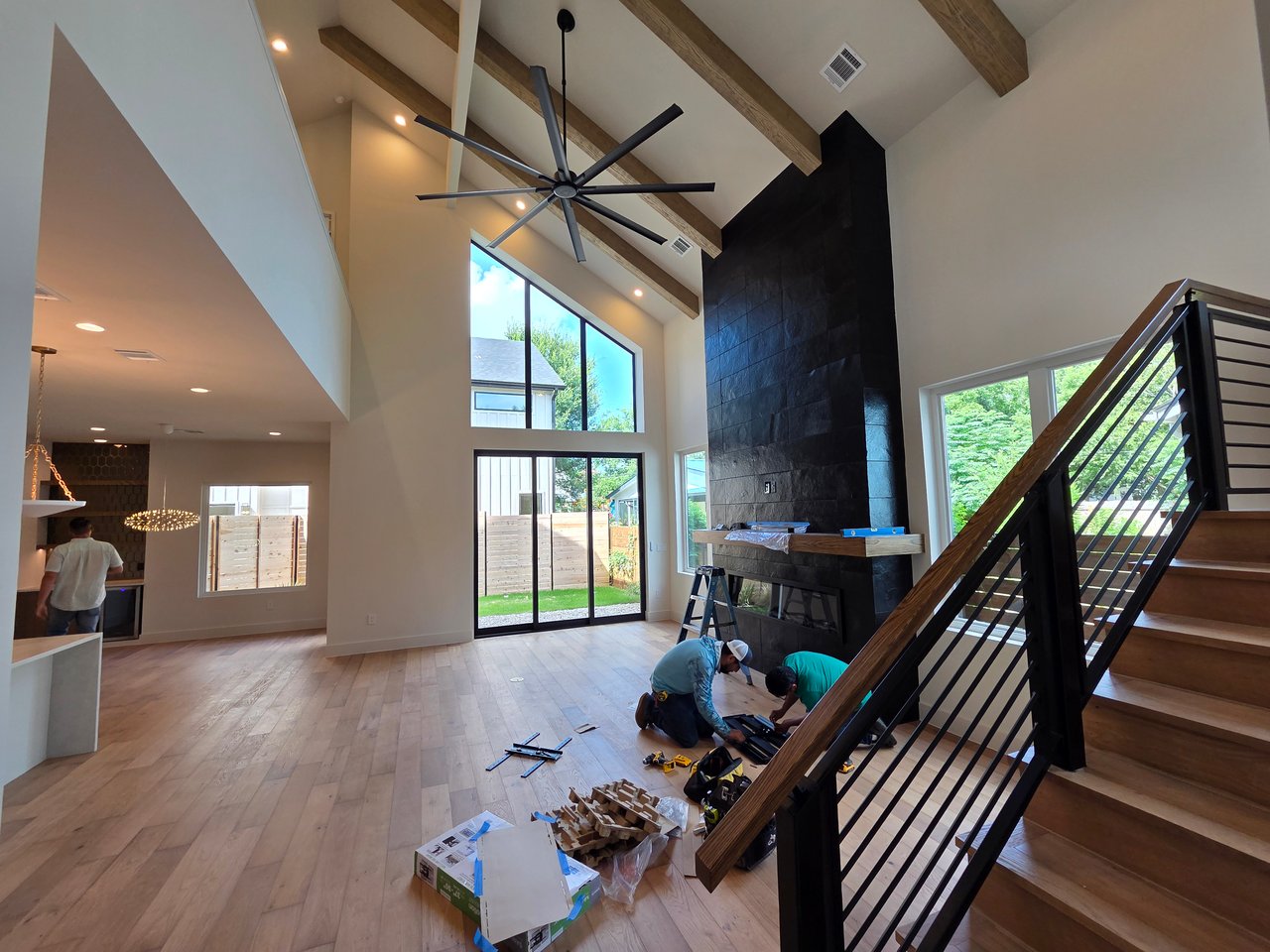 Living room under construction with a vaulted wood-beam ceiling, black fireplace, and staircase.