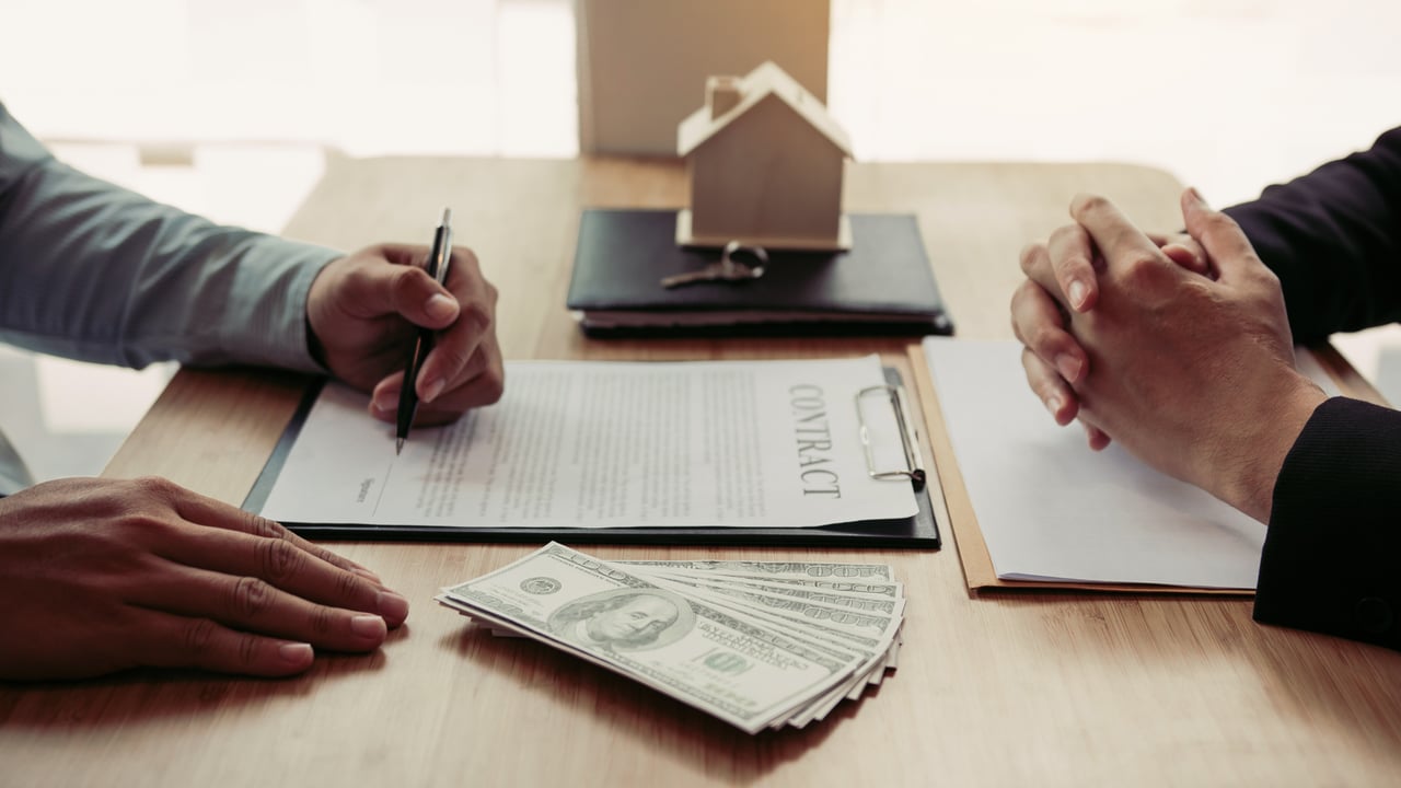 People review a real estate contract beside cash and a model house.