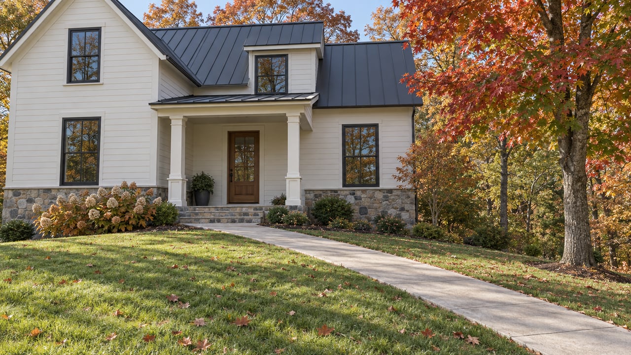 Renovated light-sided home above a sloping autumn lawn, with a stone porch, charcoal roof and red maple beside the approach.
