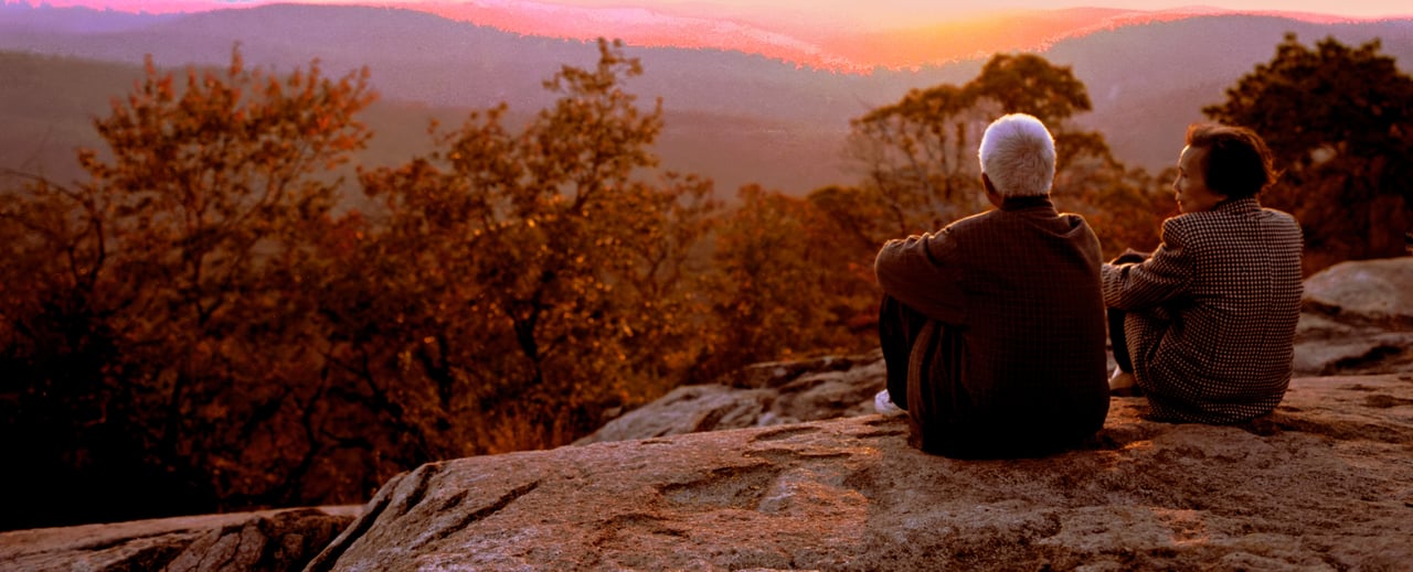 Couple seated on a rock overlook above autumn ridges at sunset in western North Carolina