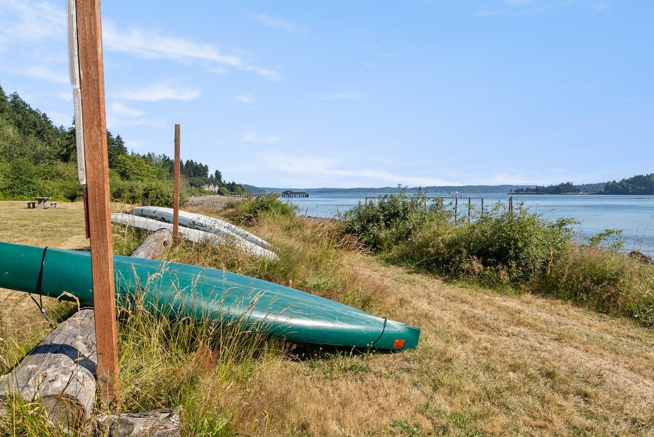 Green canoe on a grassy waterfront, with a small pier and wooded shores across the bay.