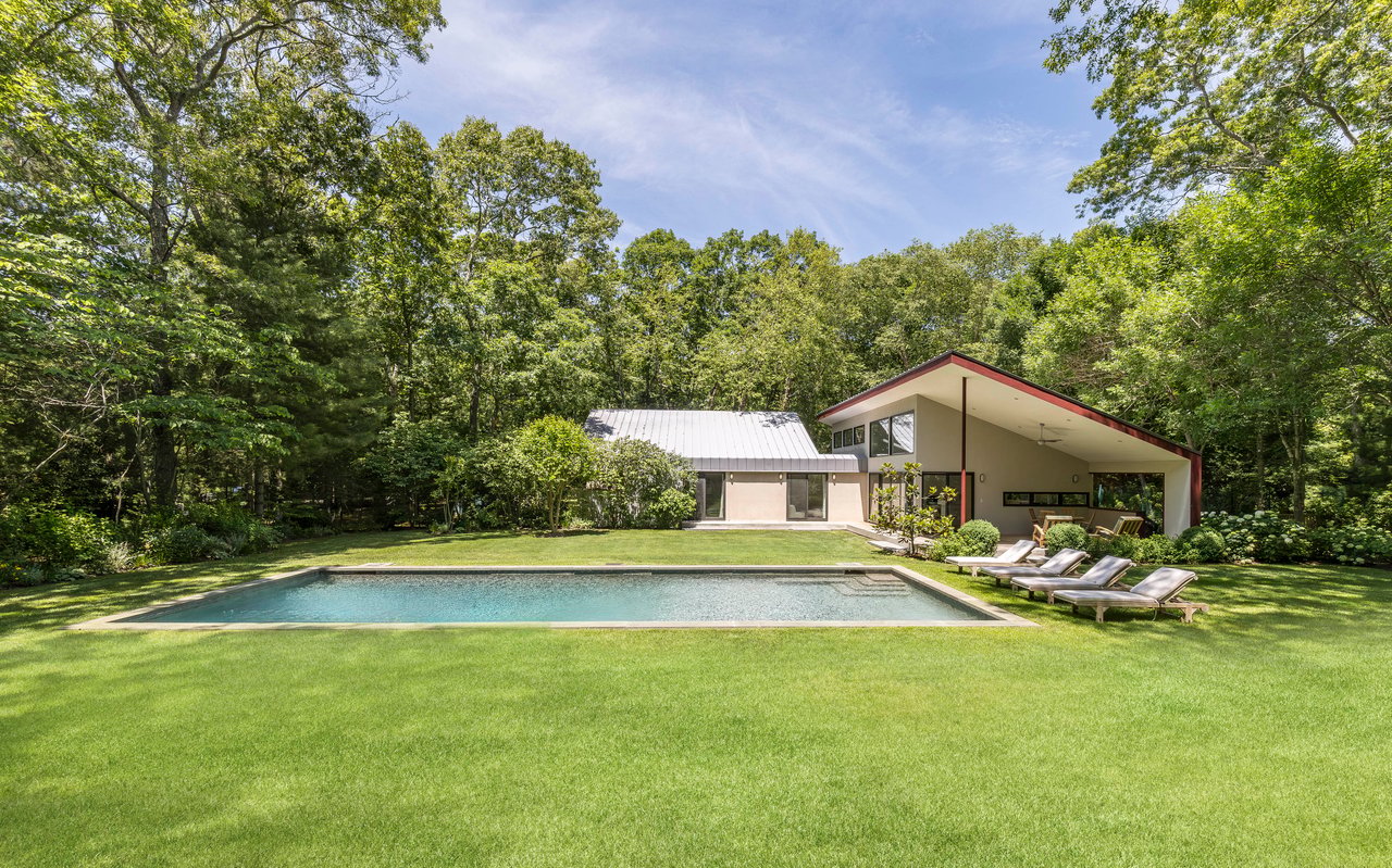 Modern East Hampton home with an angular roof, swimming pool, and wooded lawn.