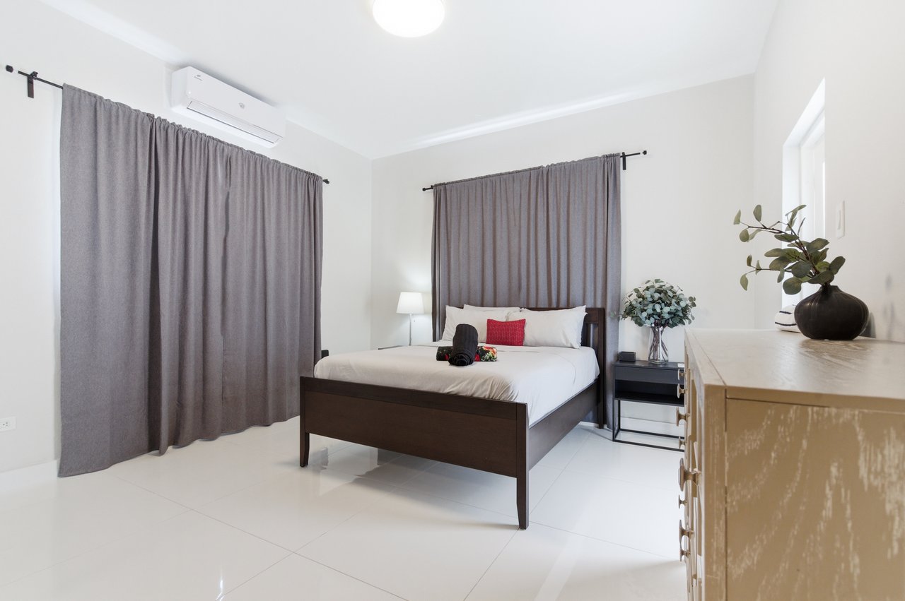 Furnished bedroom with a dark wood bed, gray curtains, and wall-mounted air conditioner.