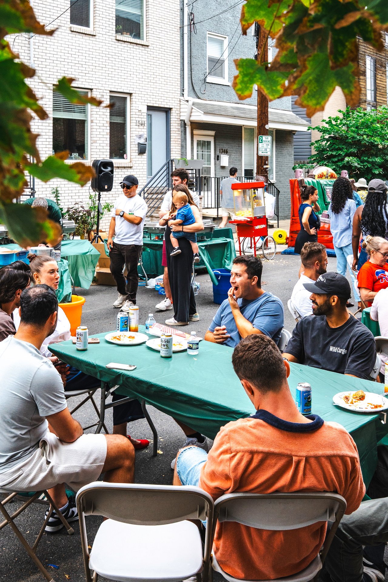 Neighbors gather around food-covered tables at a residential street block party.