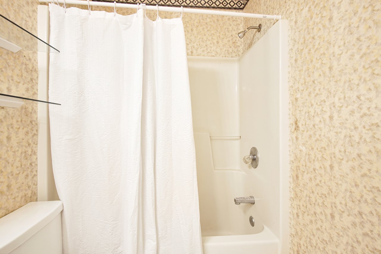 A simple white shower curtain hanging in a bathroom, providing a clean and minimalist aesthetic.