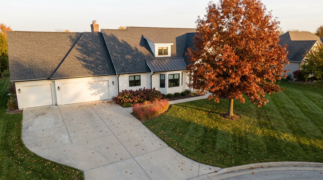 Suburban home with charcoal roof and curved driveway, beside a red-orange oak casting long shadows across the lawn.