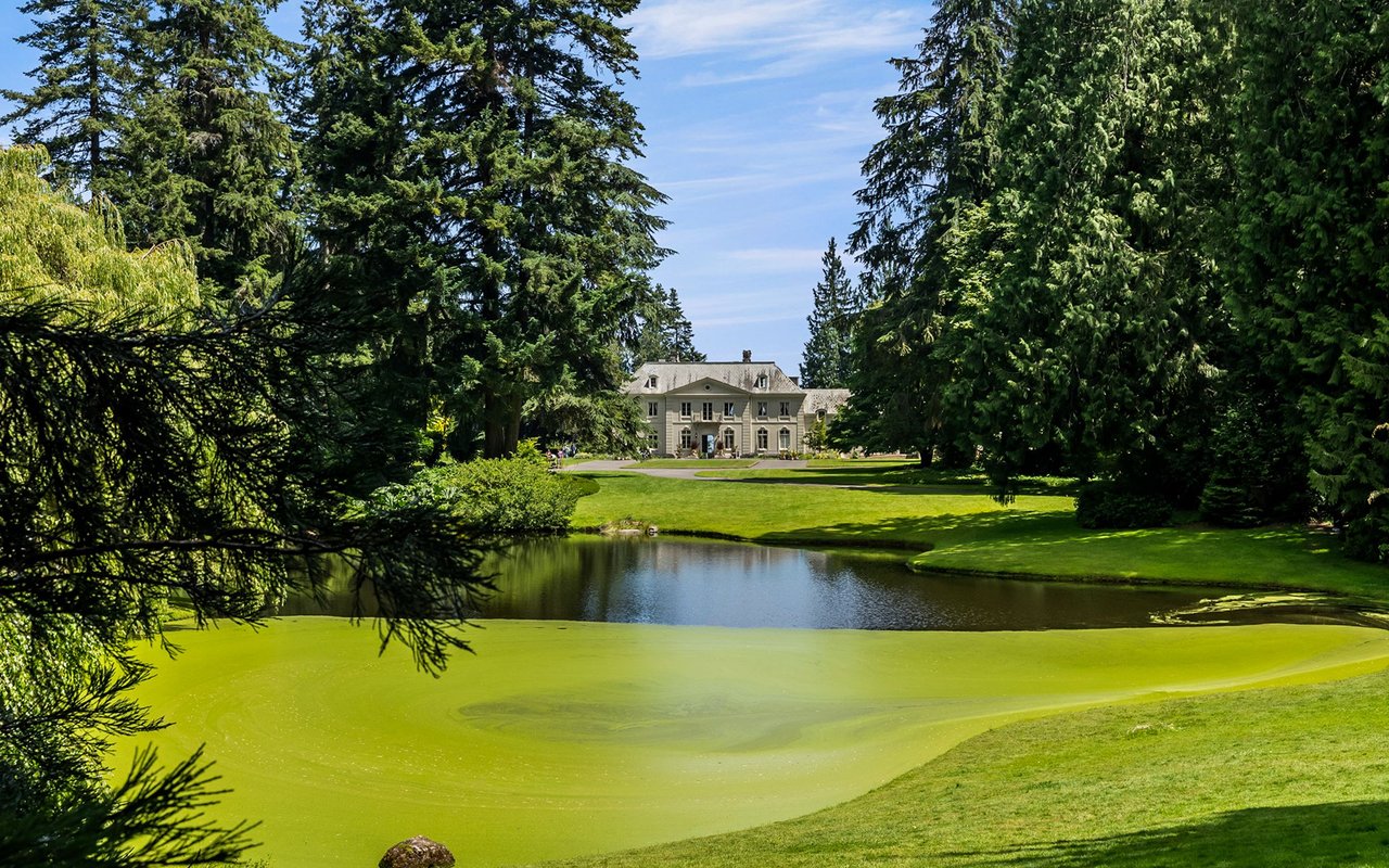 Bloedel Reserve manor house framed by evergreens across a pond and landscaped lawns.