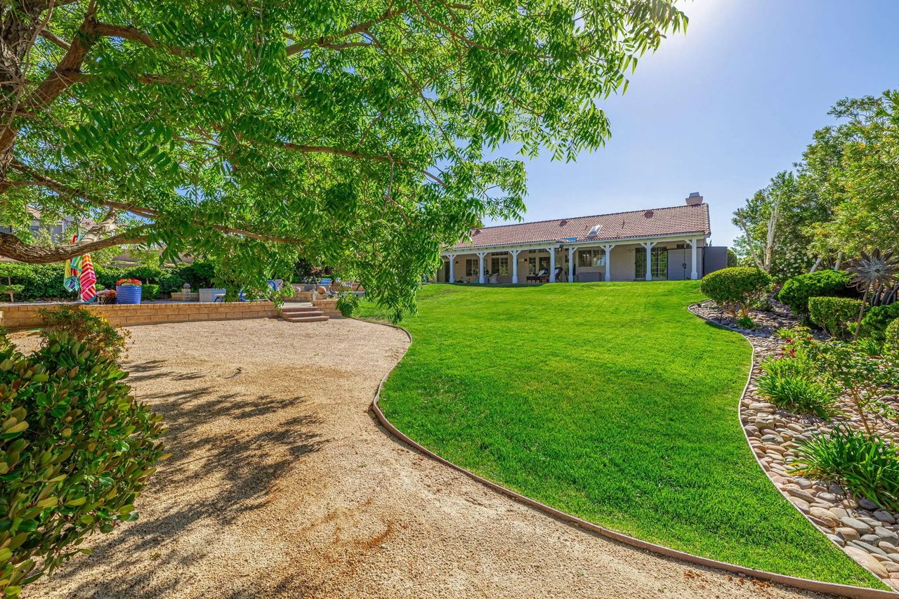 Backyard with a curved lawn, gravel path, mature shade tree, and covered patio.
