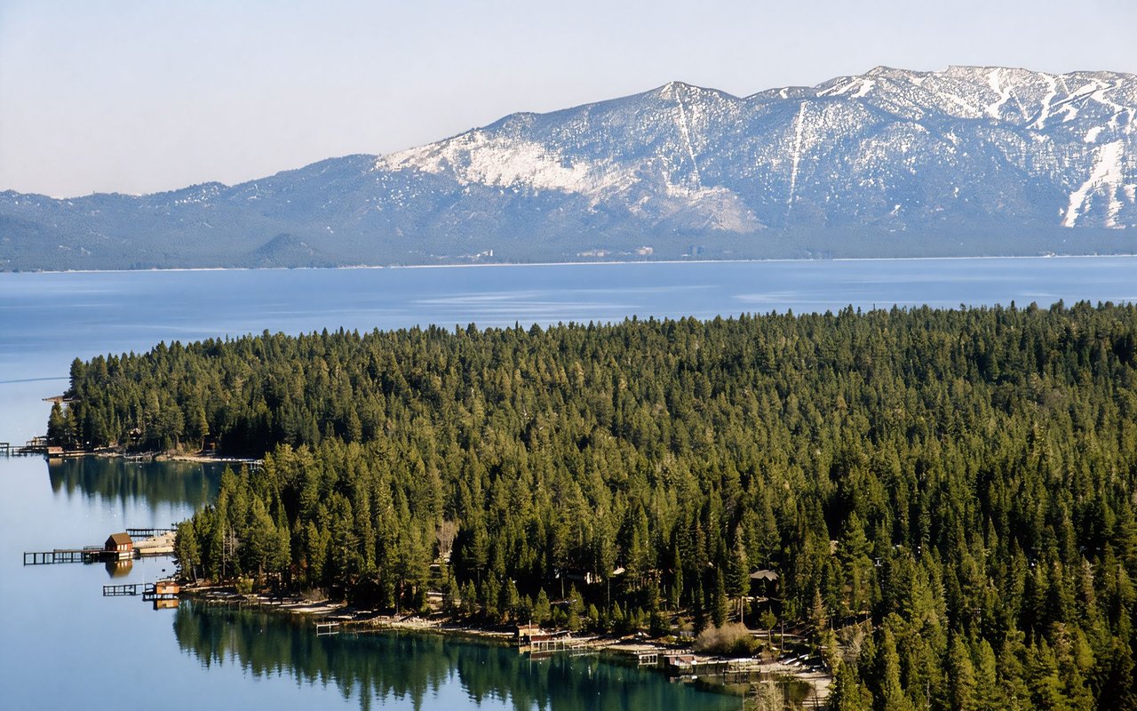 Homewood’s forested Lake Tahoe shoreline, with docks below snow-dusted mountains.