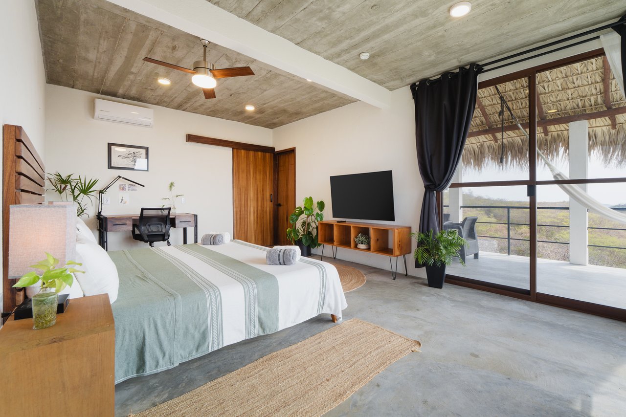 Bedroom with a king-size bed and desk beside sliding glass doors opening to a balcony.