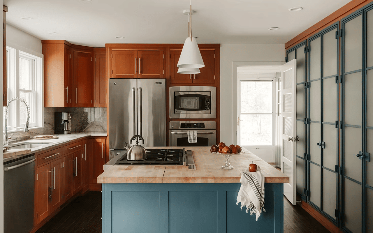 Kitchen with a blue island, gas cooktop, warm wood cabinets, and tall blue-gray pantry cabinets.