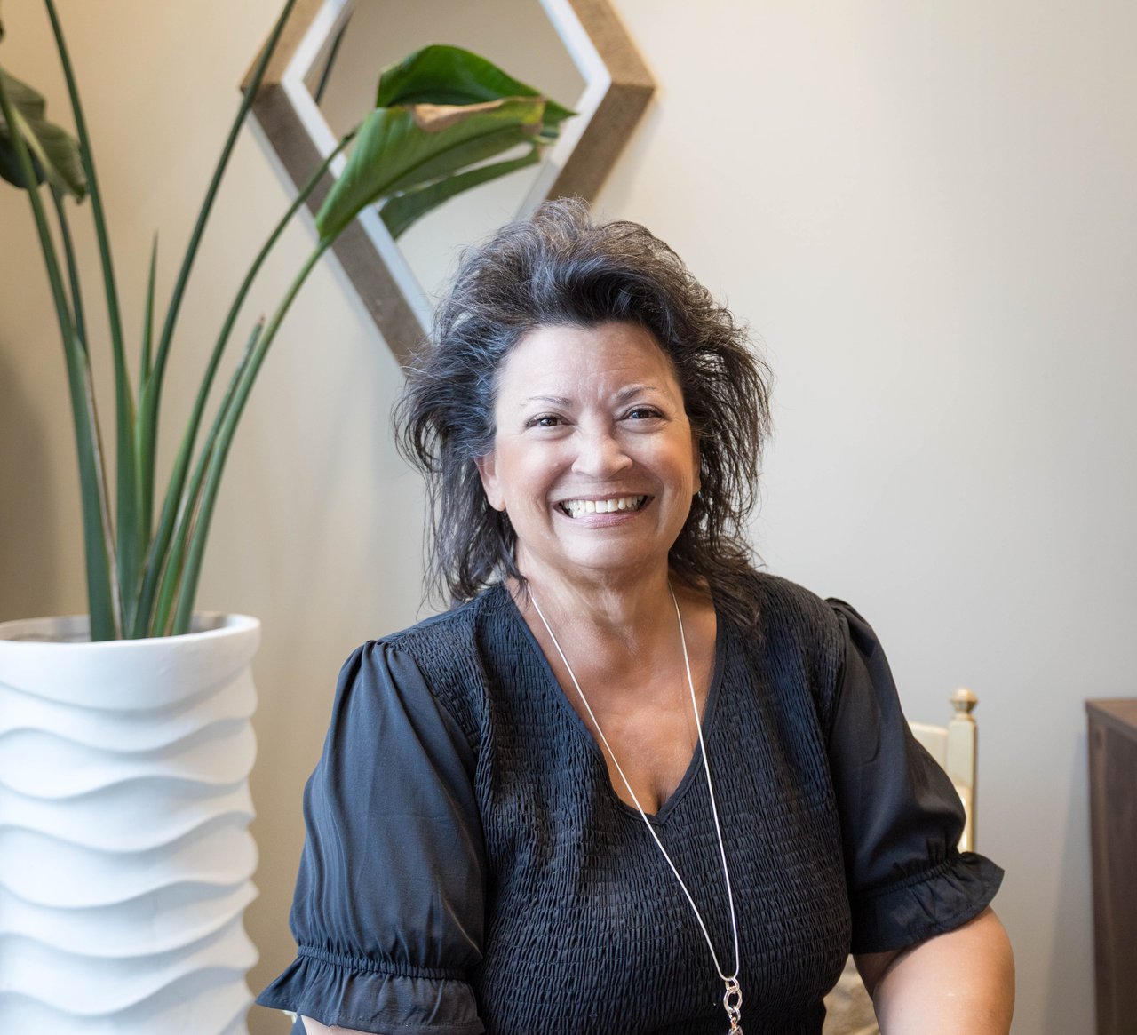Pamala Carter smiling in a black blouse beside a tall potted plant.