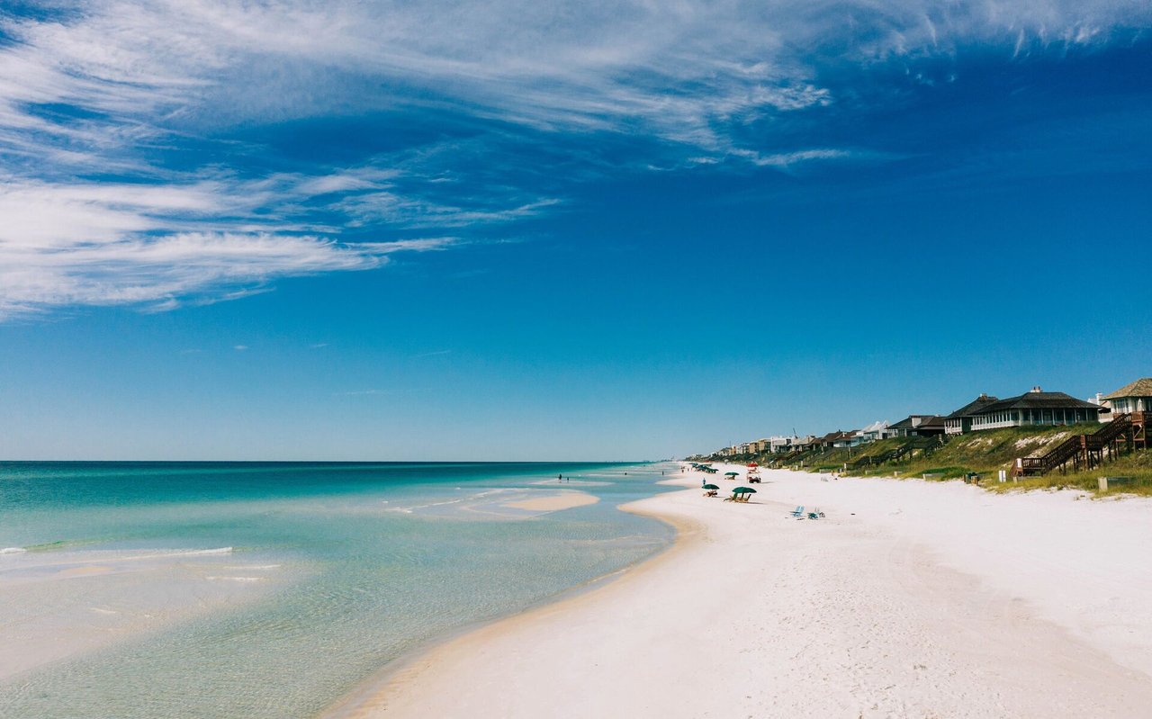 White-sand beach and turquoise water beside beachfront homes and wooden boardwalks.