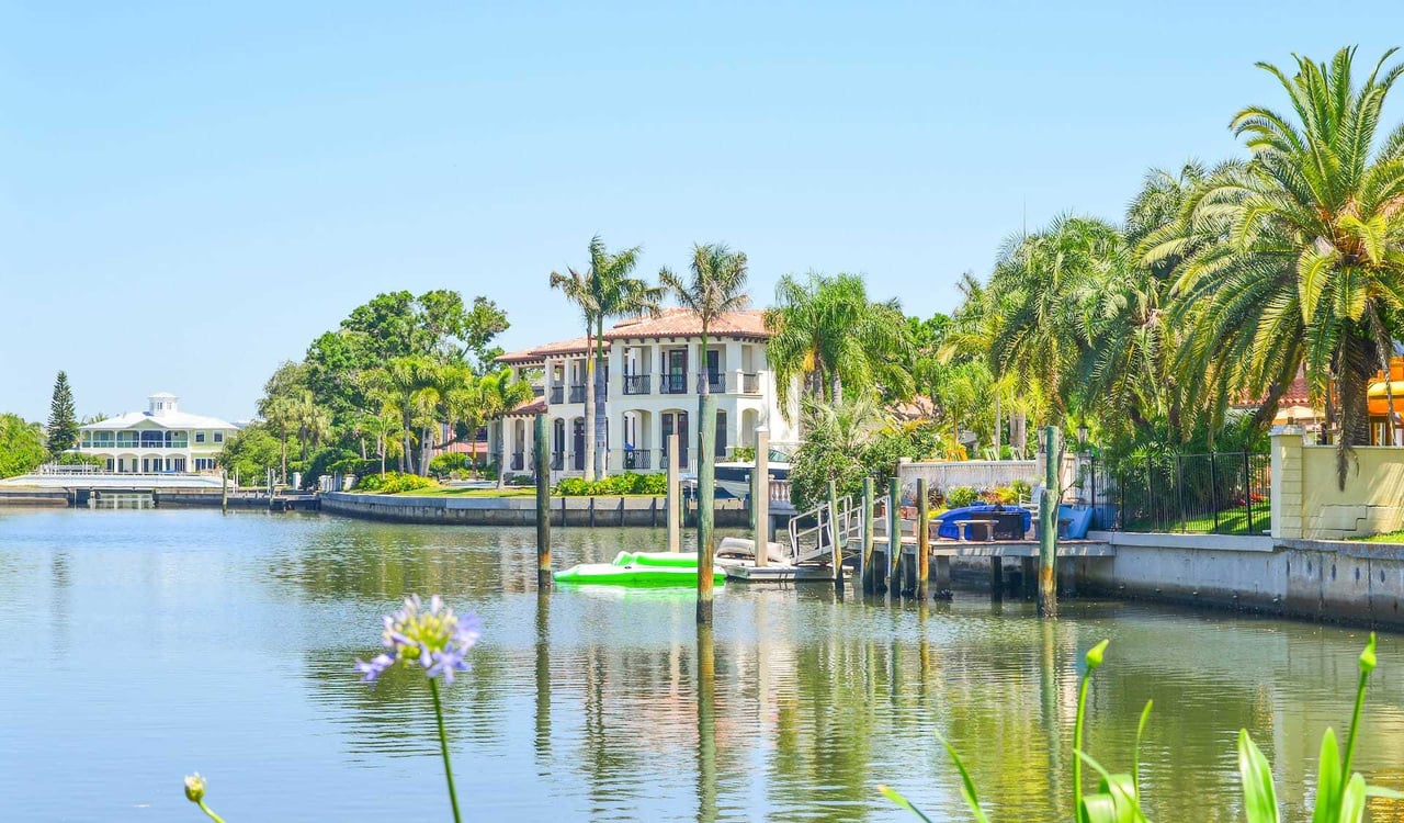 Waterfront homes line a calm canal, with private docks, palm trees, and a green watercraft.