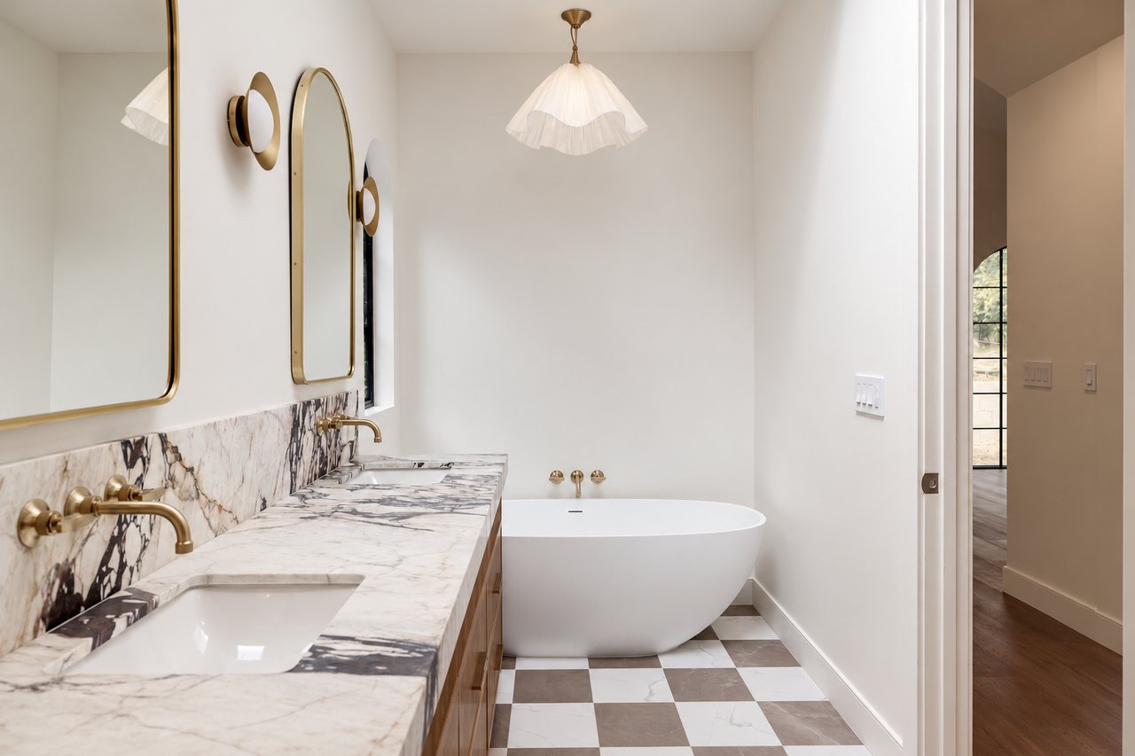 Bathroom with a freestanding tub, marble vanity, brass fixtures, and checkerboard floor.