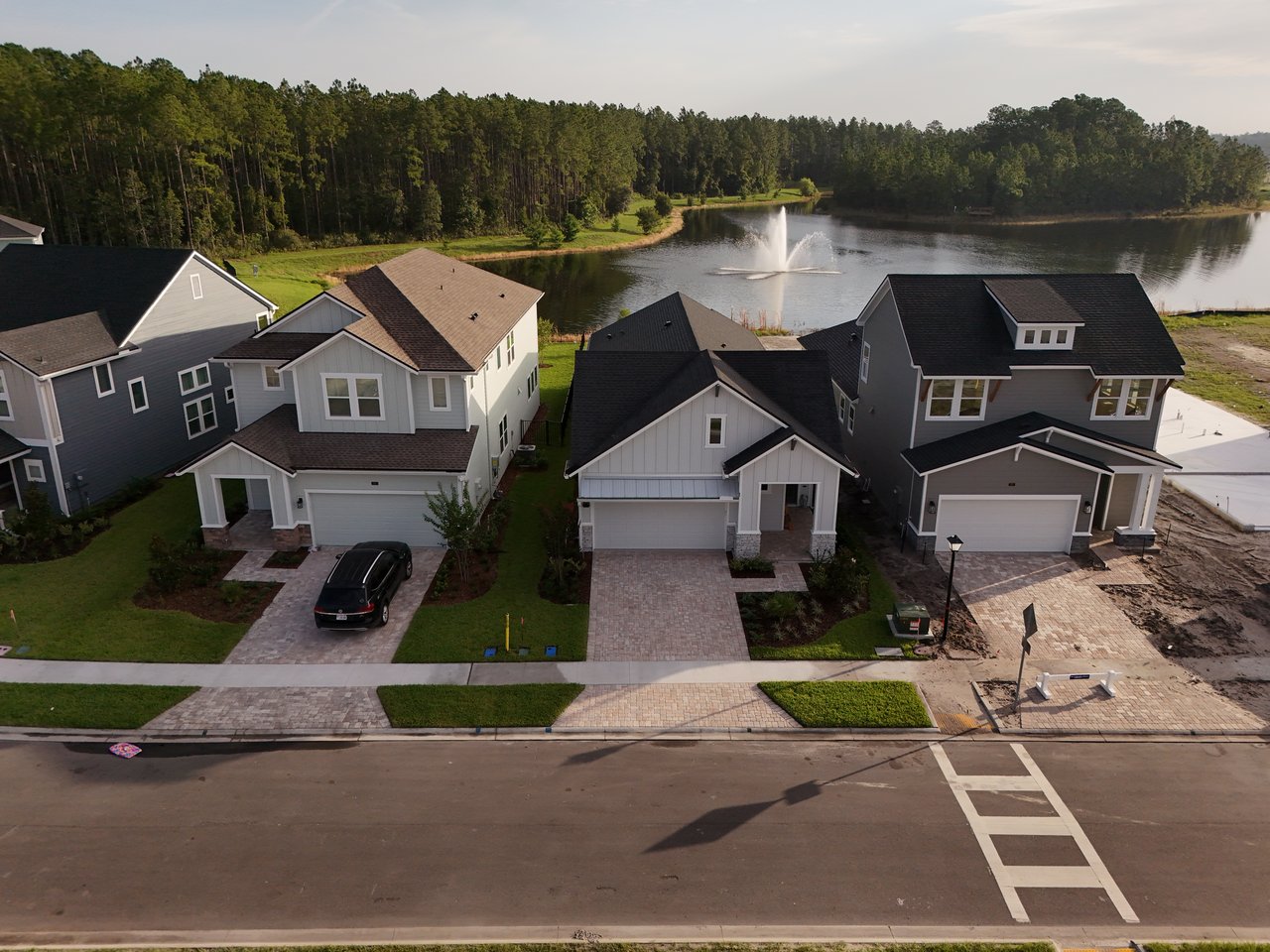 Aerial view of homes beside a lake with a fountain and wooded shoreline.